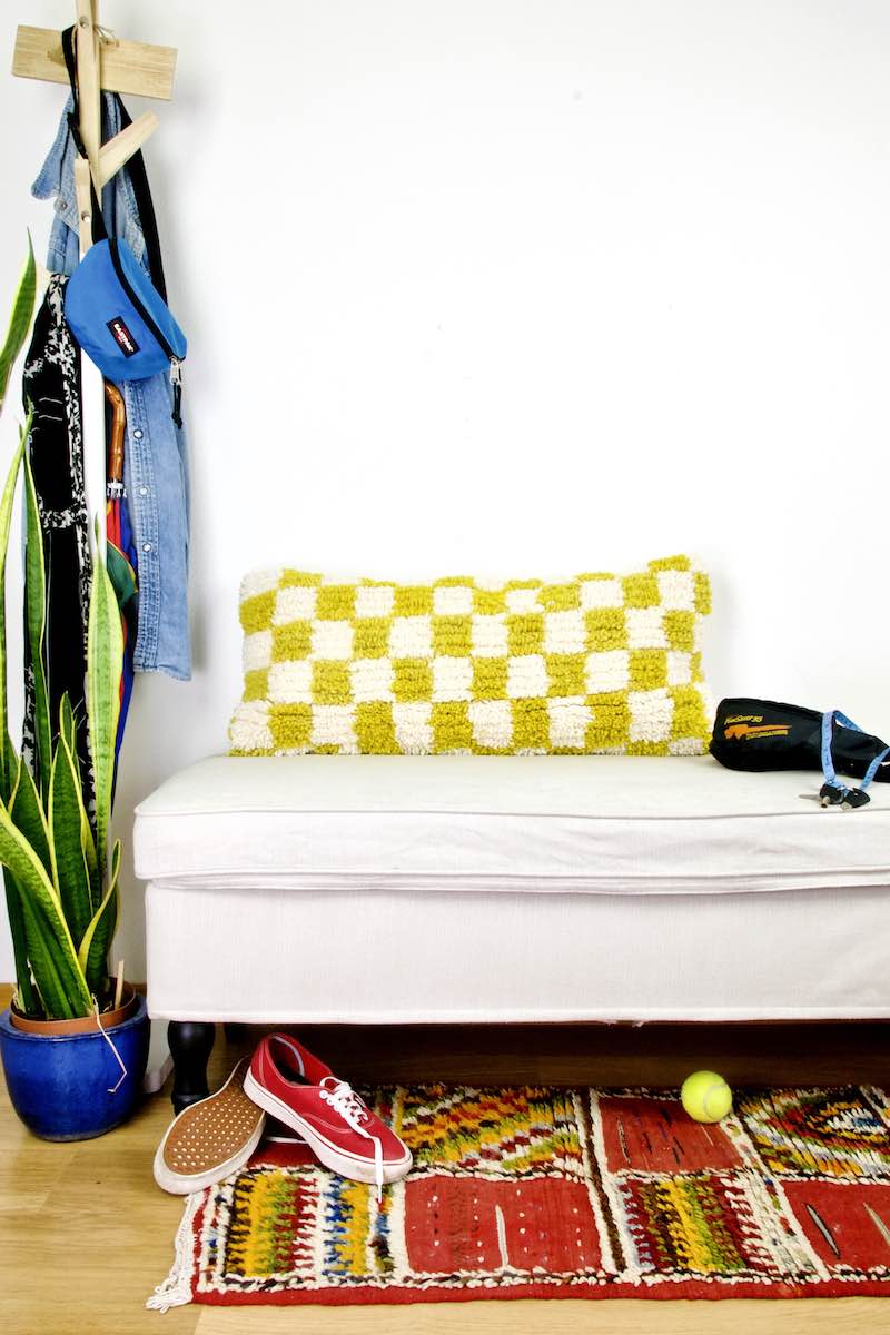 Yellow white checkered Beni Ourain Berber lumbar pillow on a white bench in the living room.