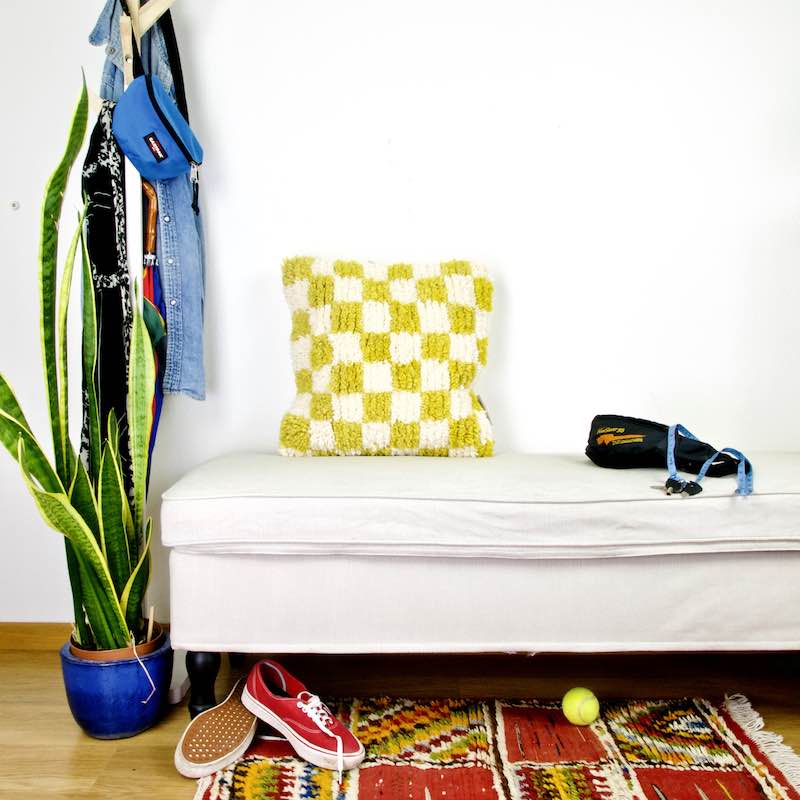 Yellow white checkered Beni Ourain Berber pillow on a white bench.