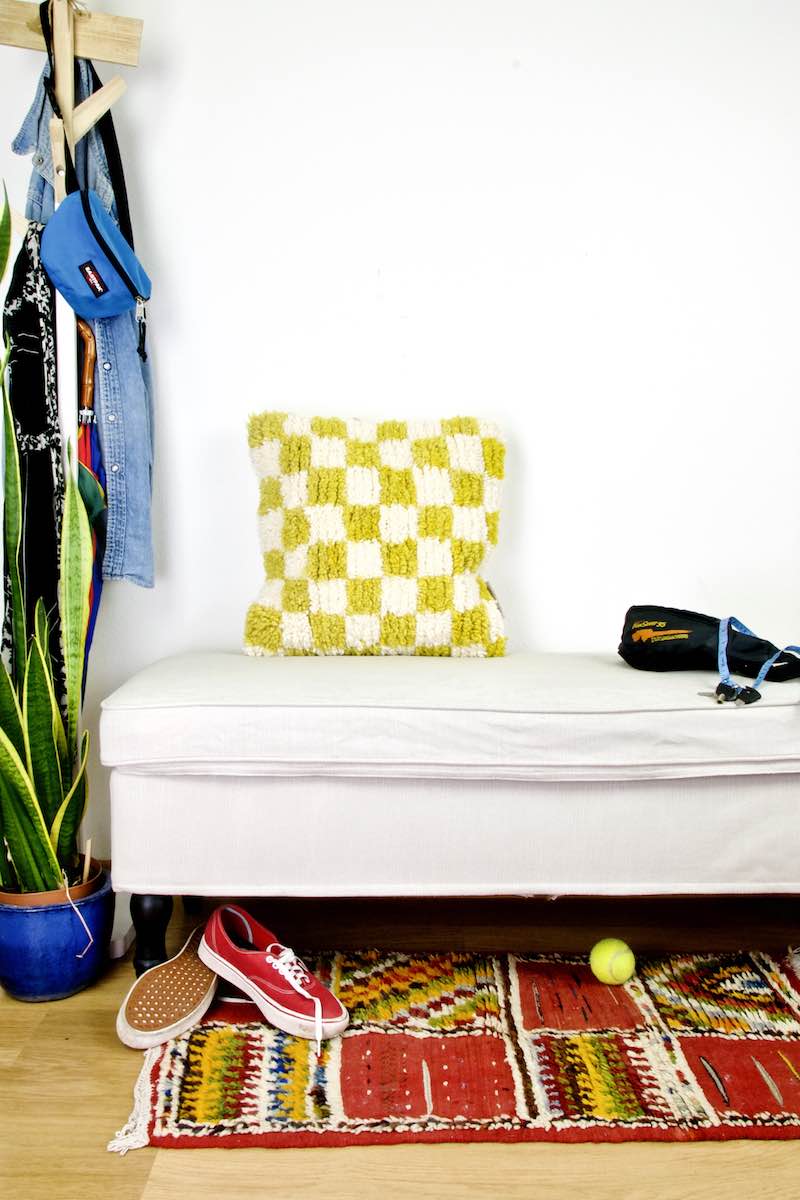 Yellow white checkered Beni Ourain pillow on a white bench in the living room.