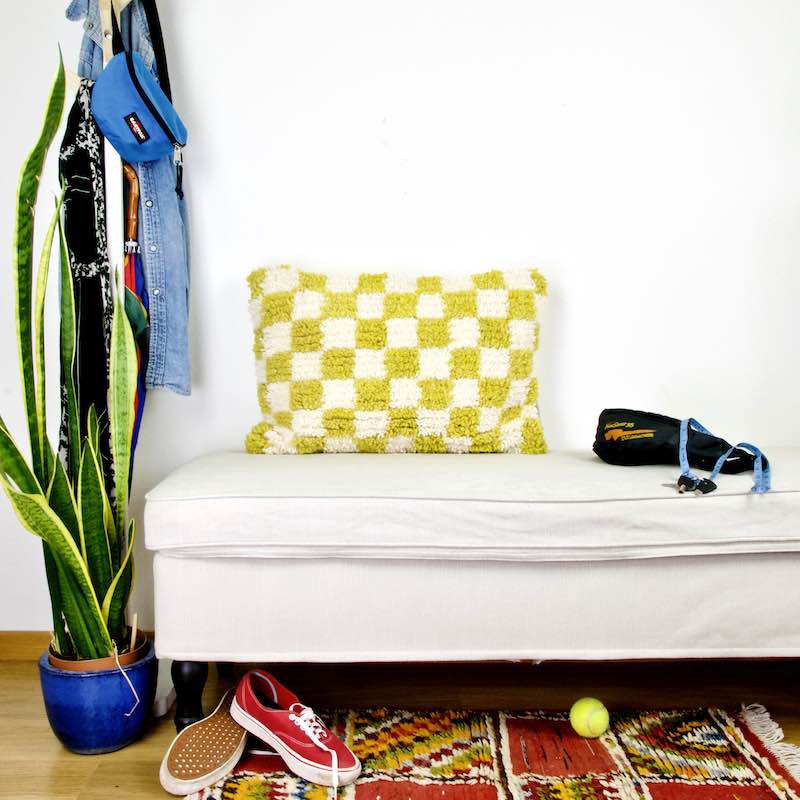 Yellow white checkered Beni Ourain Berber pillow on a white bench.