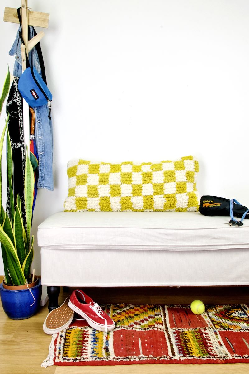 Gelb-weiss kariertes Beni Ourain Fluffikon Wollkissen auf einer weissen Bank. Die Kissen Grösse ist 35x70 cm.