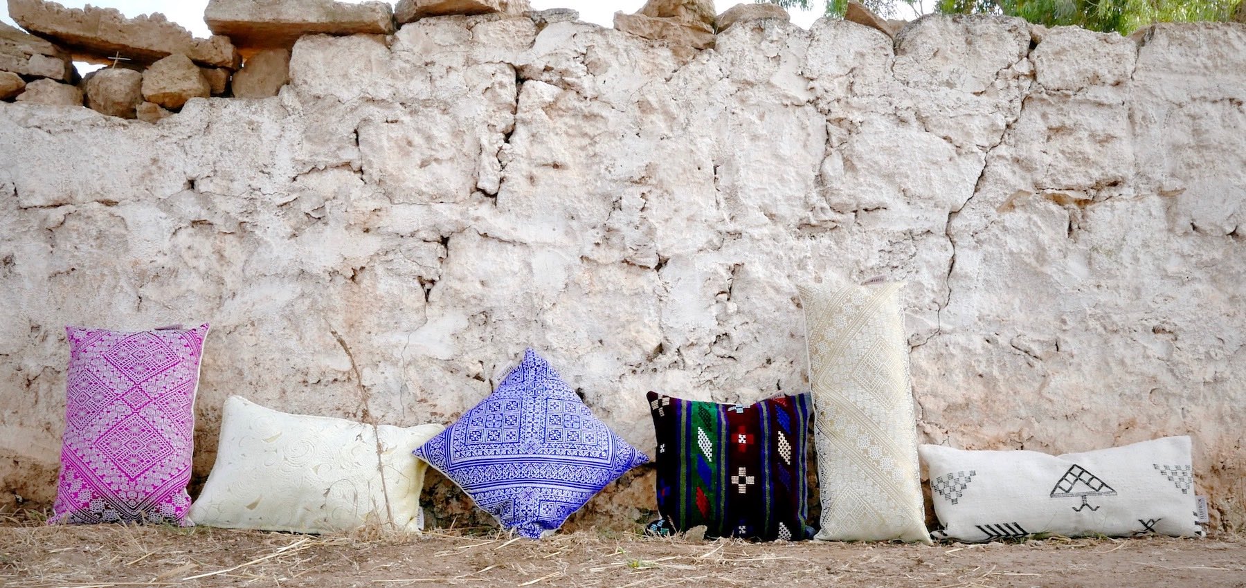 Six decorative Moroccan pillows in front of a stone wall.