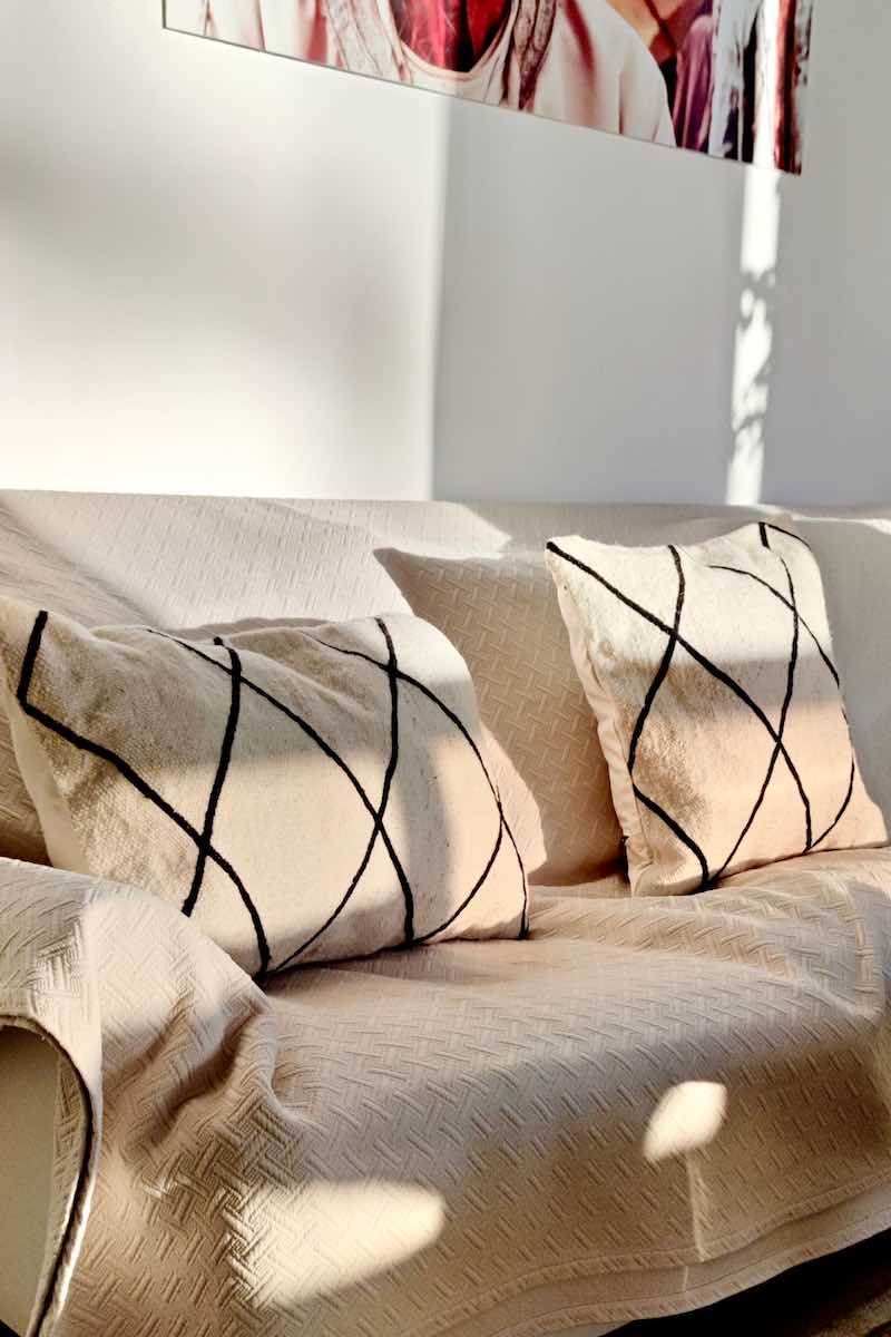 Zwei Fluffikon Kelim Beber Kissen aufgenommen bei natürlichem Sonnenlicht. Die Kissen liegen auf einem weissen Sofa.