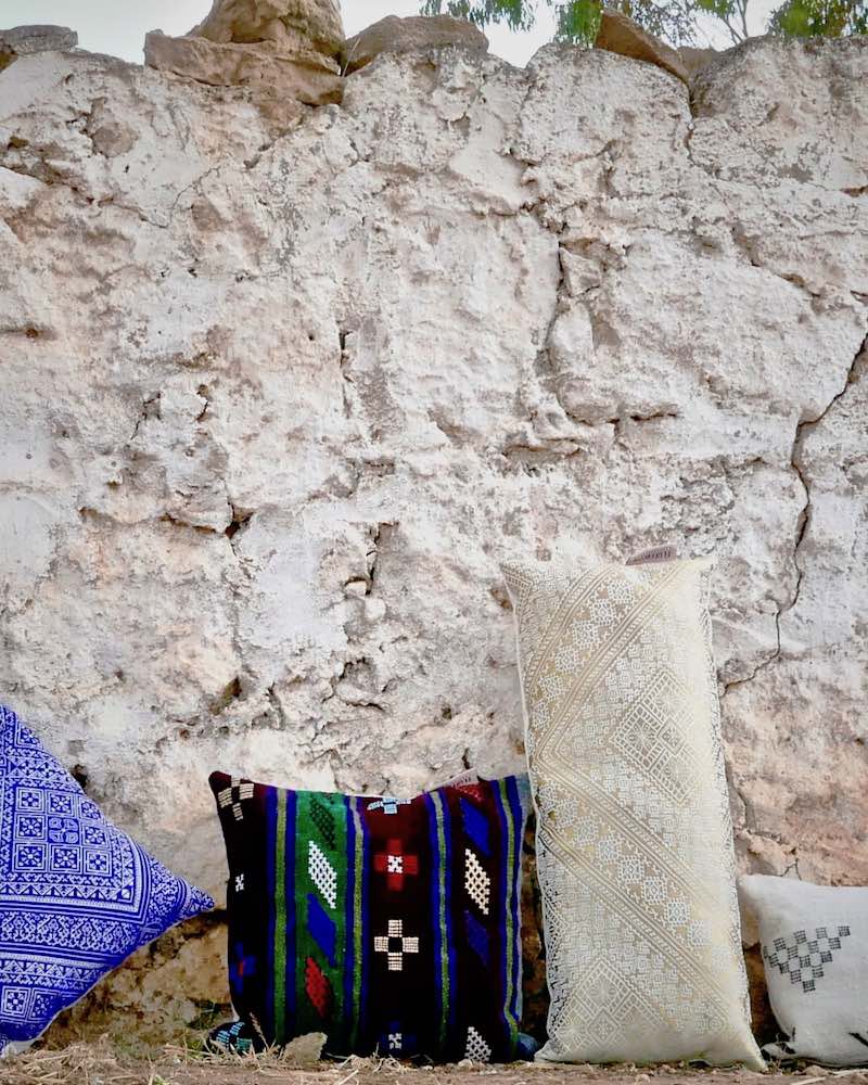 Four Fluffikon Moroccan pillows standing outside in front of a stone wall. 