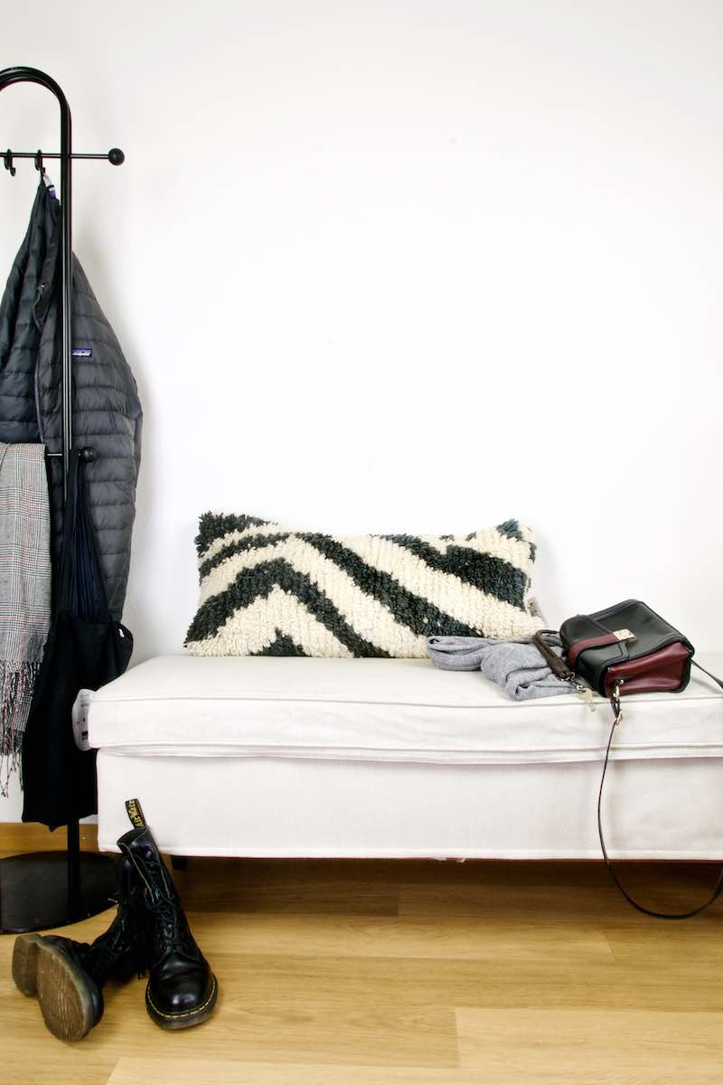 A black and white vintage Fluffikon rug pillow on a white bench.