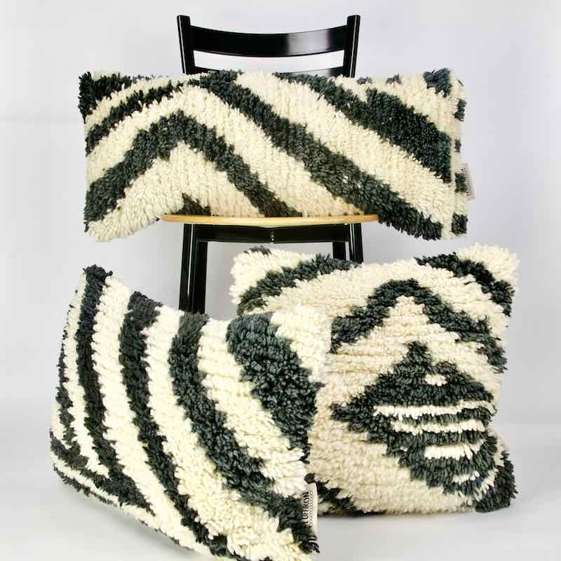 Drei vintage Teppichkissen aus Wolle. Zwei der schwarz weissen Kissen stehen vor einem Stuhl. Eines steht auf dem Stuhl.