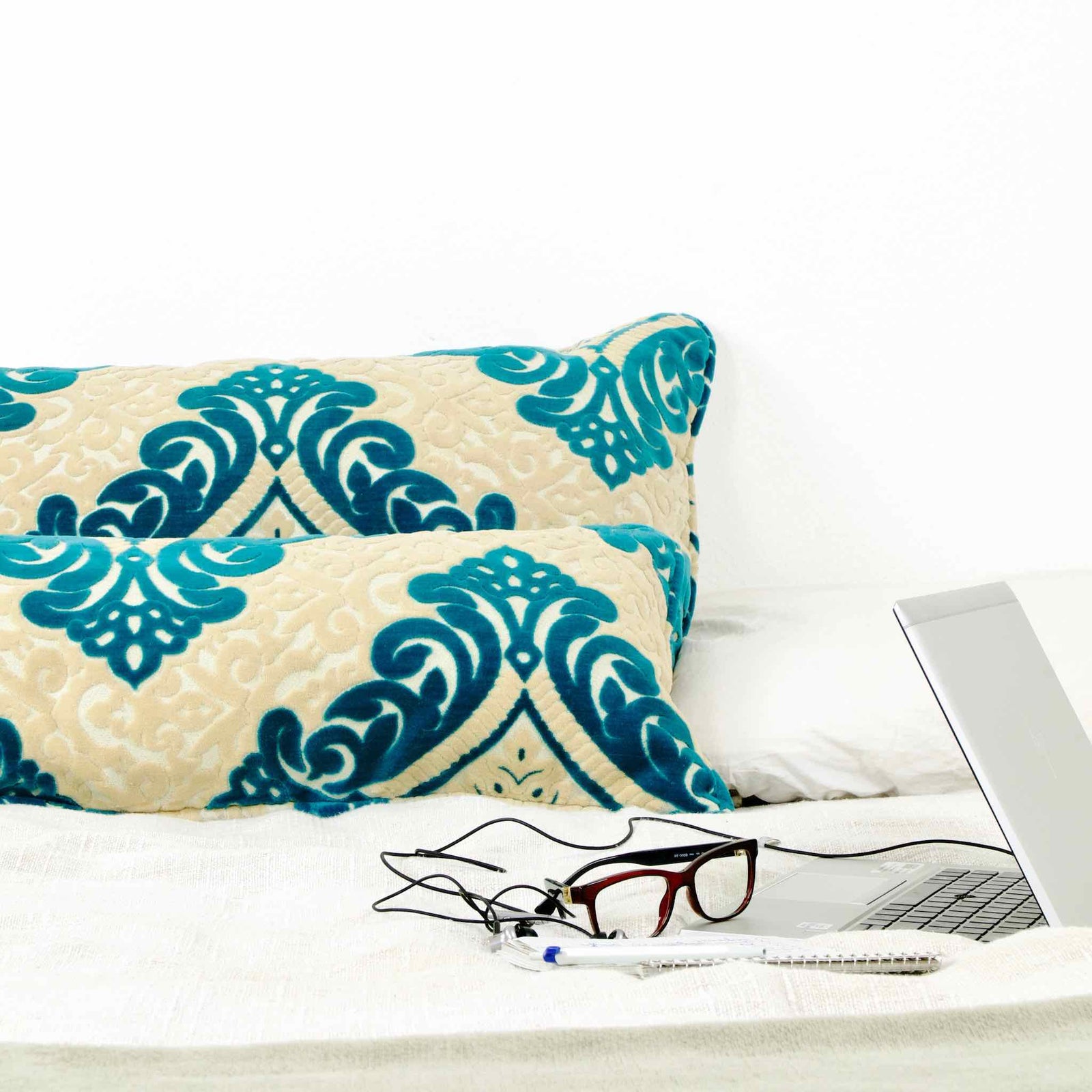 Two large throw pillows with green beige moroccan patterns on white bed.