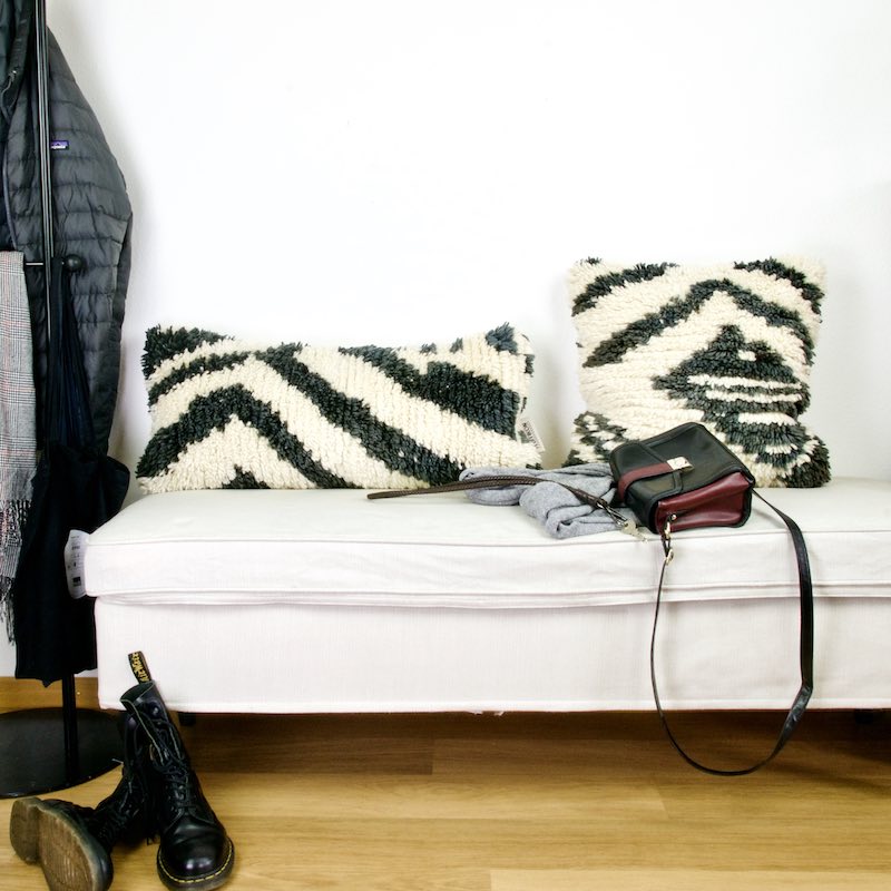 Two black and white vintage Fluffikon rug pillows on a white bench. The pillows are made from Moroccan wool rugs.