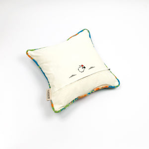 Blue Fluffikon decorative square pillow made from shiny brocade with colourful flowers embroidery. The back of the pillow is shown. Pillow is on the ground.