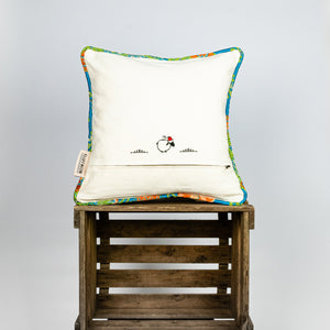 Blue decorative square pillow made from shiny brocade with colourful flowers embroidery. Back of the pillow is shown. Pillow stands on a wooden box.