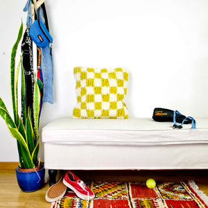 Beni Ourain Fluffikon pillow with yellow white checkered pattern. The pillow is made from wool. It stands on a white bench..