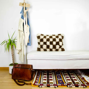 Brown checkered Fluffikon throw pillow on a white bench. The Moroccan pillow was made from a Berber Beni Ourain wool rug.