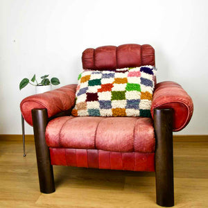 Colorful checkered Fluffikon throw Pillow on a red leather chair