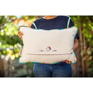 Blue Fluffikon decorative square pillow made from shiny brocade with colourful flowers embroidery. The back of the pillow is shown. Woman holds pillow.