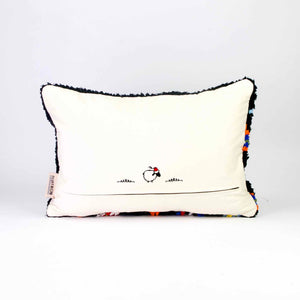 the back of a black Fluffikon Boucherouite throw pillow. The upcycled pillow has colorful patterns embedded in the black fabric.