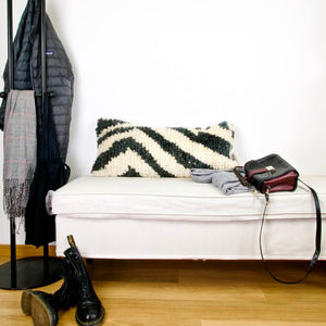 Wool vintage Fluffikon rug pillow standing on a white bench. The lumbar pillows is black and white.