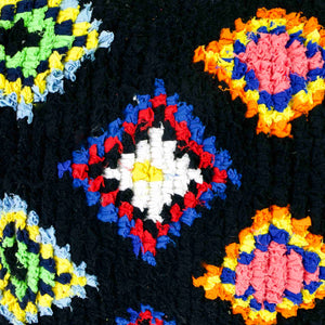 Zoom on a black Fluffikon Boucherouite throw pillow. The upcycled pillow has colorful patterns embedded in the black fabric.