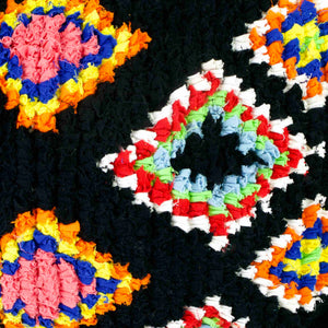 Zoom on a black Fluffikon Boucherouite throw pillow. The upcycled pillow has colorful patterns embedded in the black fabric.