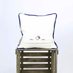 The back of a sapphire blue velvet throw pillow with piped edges. The pillow stands on a wooden box.