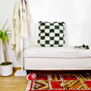 Checkered Moroccan Fluffikon pillow standing on a white bench.