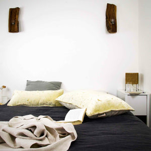 Two Fluffikon oversized lumbar pillows made from beige velvet with golden threads. The pillows is lying on bed with an open book in front of it.