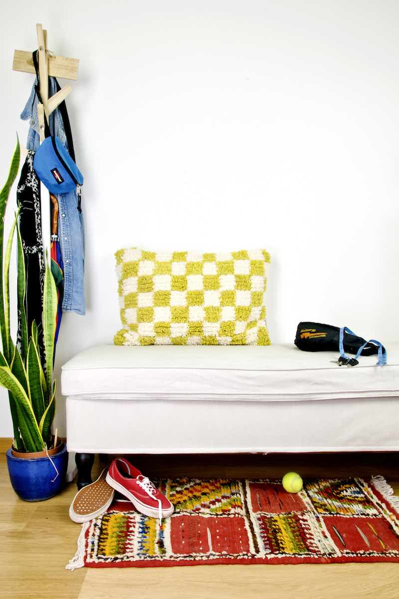 Yellow white checkered Beni Ourain Berber pillow on a white bench.