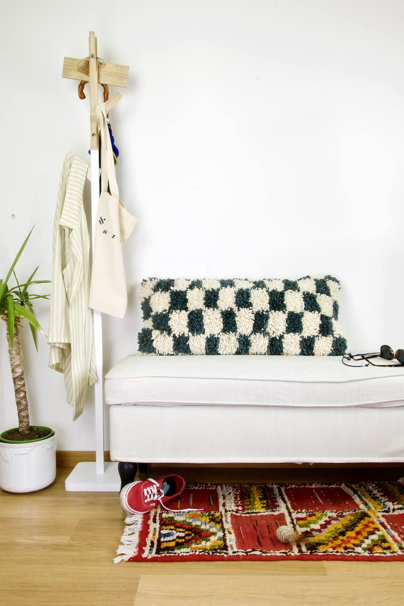 A Checkered Moroccan lumbar wool pillow on a white bench. The pillow is grey-blue white/beige checkered. 