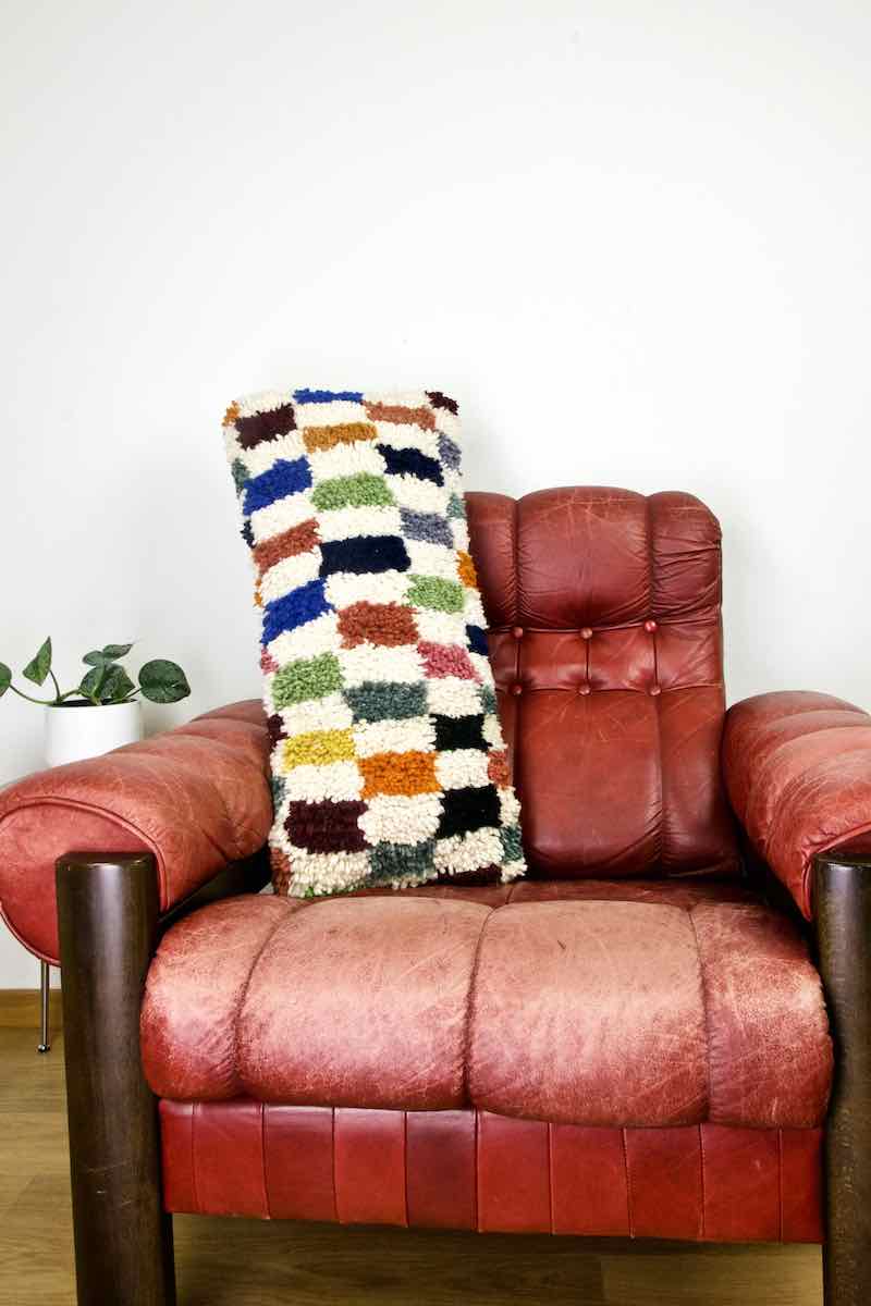 A colorful checkered Fluffikon lumbar pillow on a red leather chair.