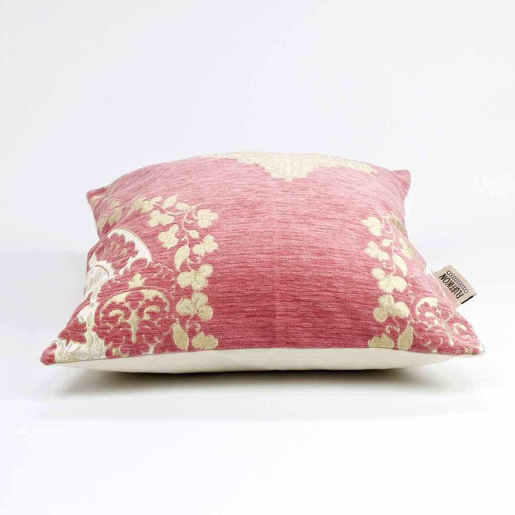 Liegendes rosa pink Dekokissen mit floralem Muster aus goldenen Blumen.