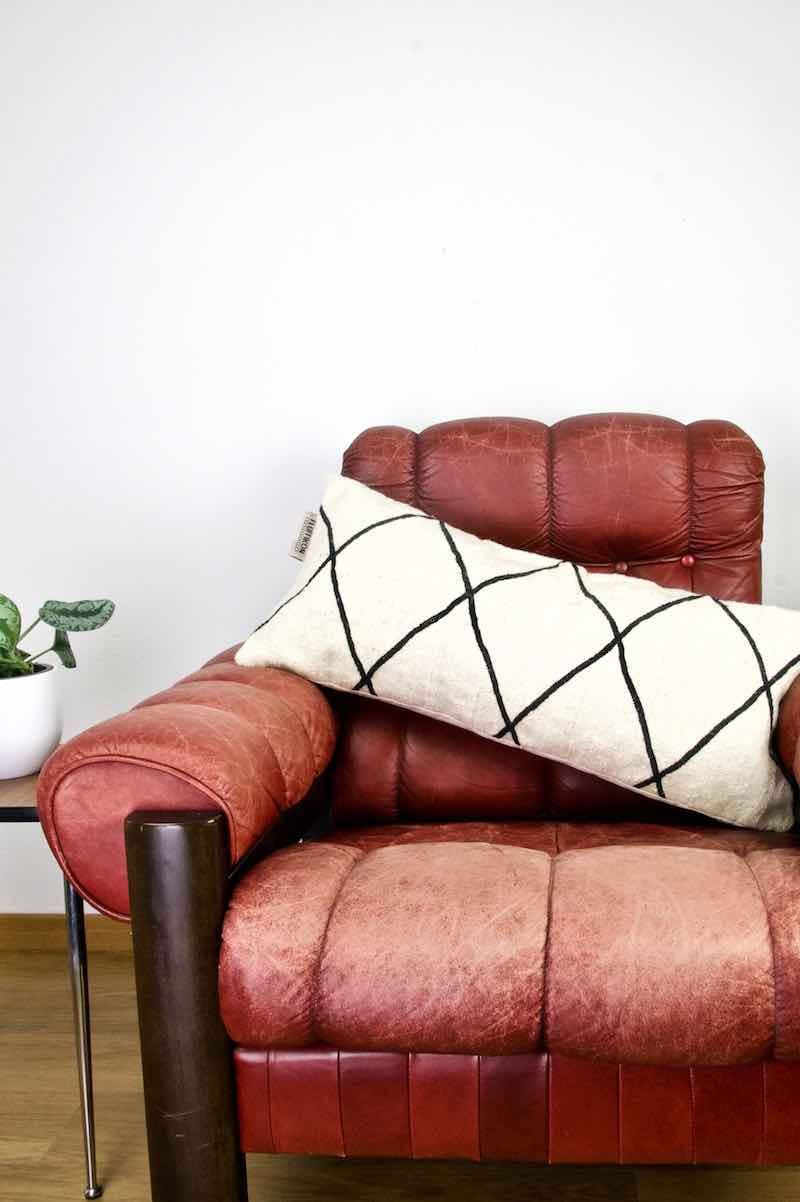 A Fluffikon Kelim throw pillow made from a black and white Kilim rug on a red leather chair. 