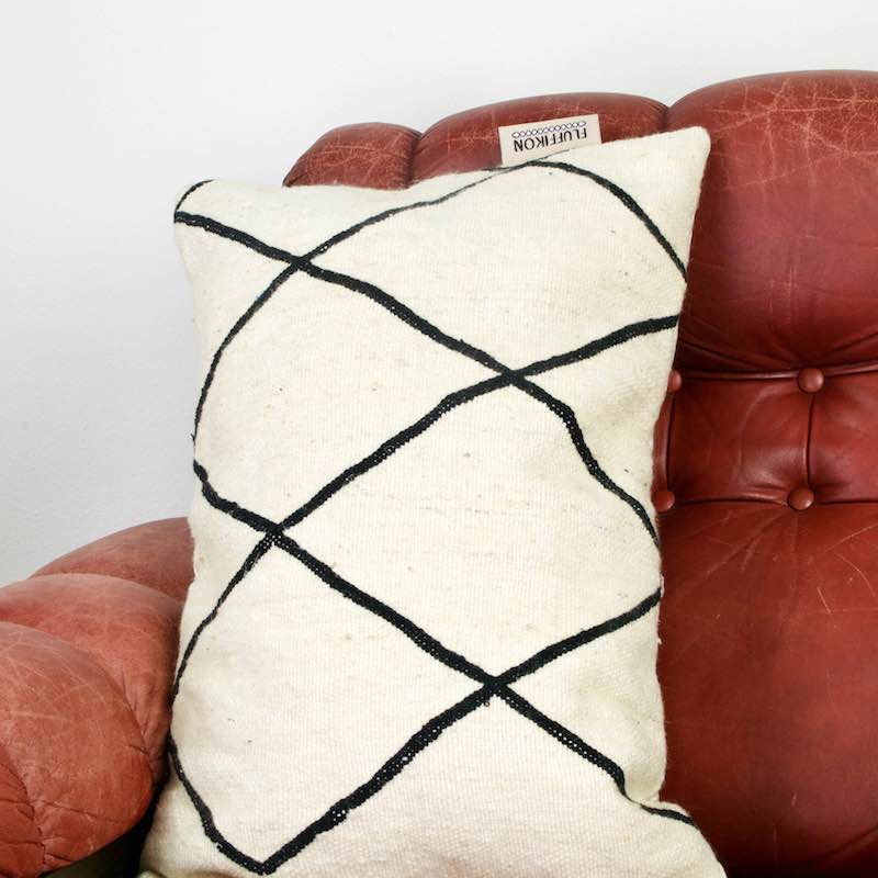 Black and white Fluffikon Kilim throw pillow on a vintage red leather chair.