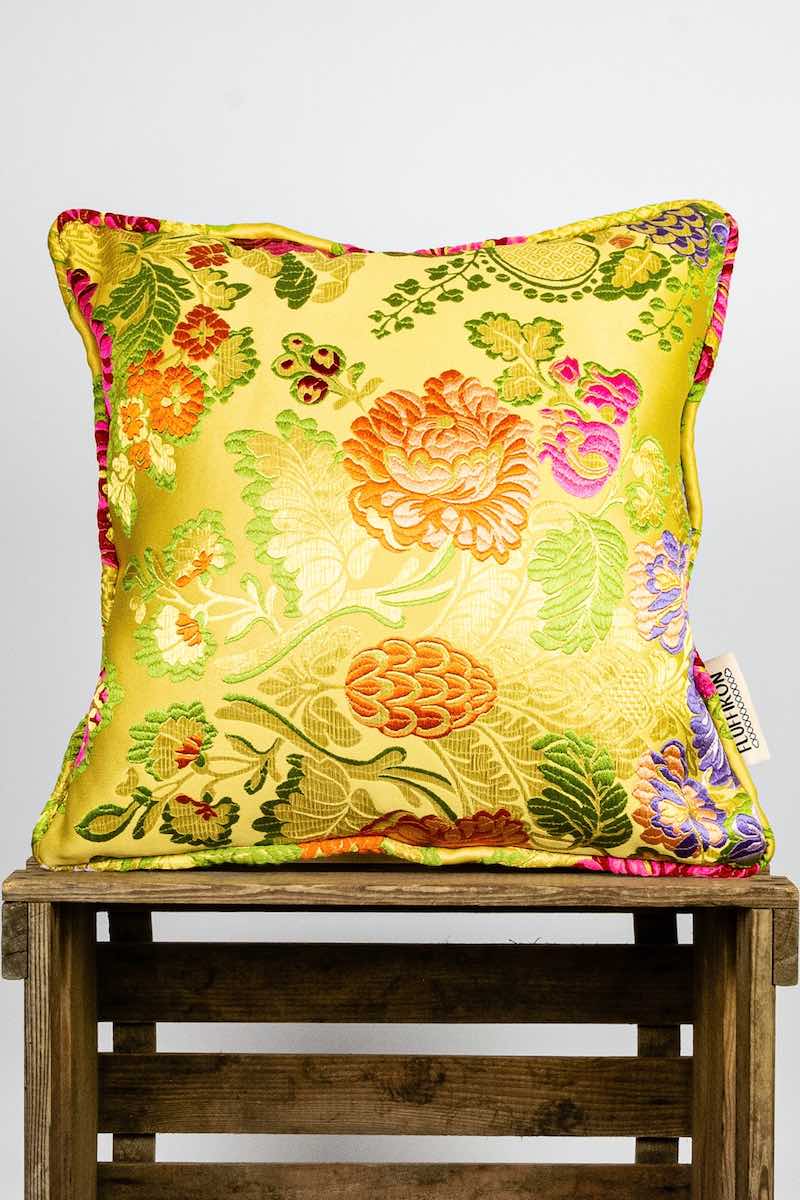 Yellow/Gold Fluffikon brocade pillow standing on a wooden box.