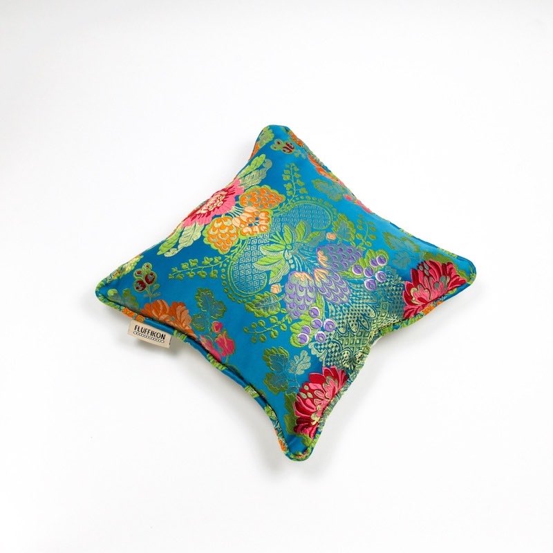 Blue brocade cushion in front of white background.