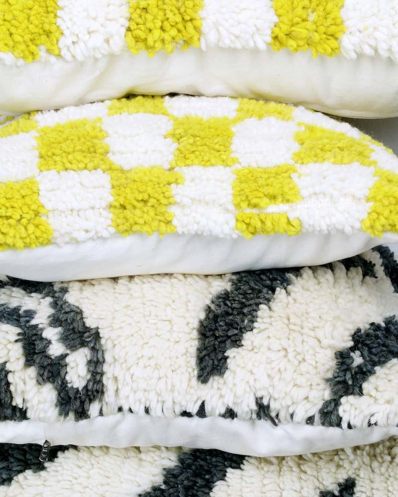 Zwei gelbe und zwei schwarz-weisse Berber Kissen aus Wolle aufeinander.