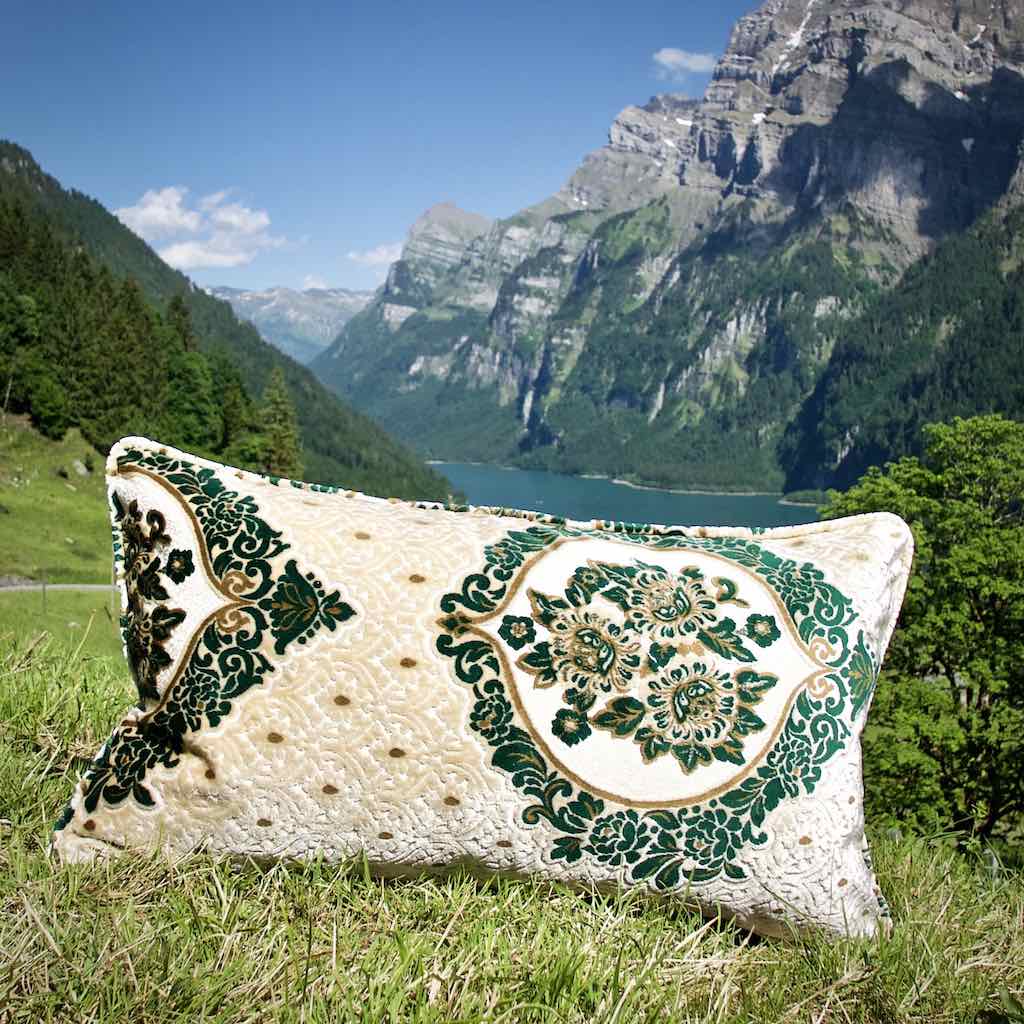 Grosses  Sofakissen mit marokkanischen Mustern in den Schweizer Bergen. Das Kissen auf einer Wiese vor einem blauem See.