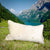 Grosses beiges Sofakissen in den Schweizer Bergen. Das Kissen auf einer Wiese vor einem blauem See.