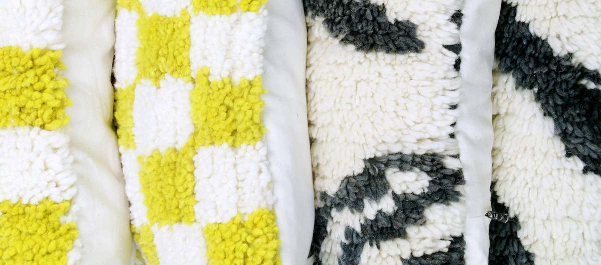 Zwei gelbe und zwei schwarz-weisse Berber Kissen aus Wolle nebeneinander. Die Kissen sind aus einem marokkanischen Berber Teppich gefertigt.