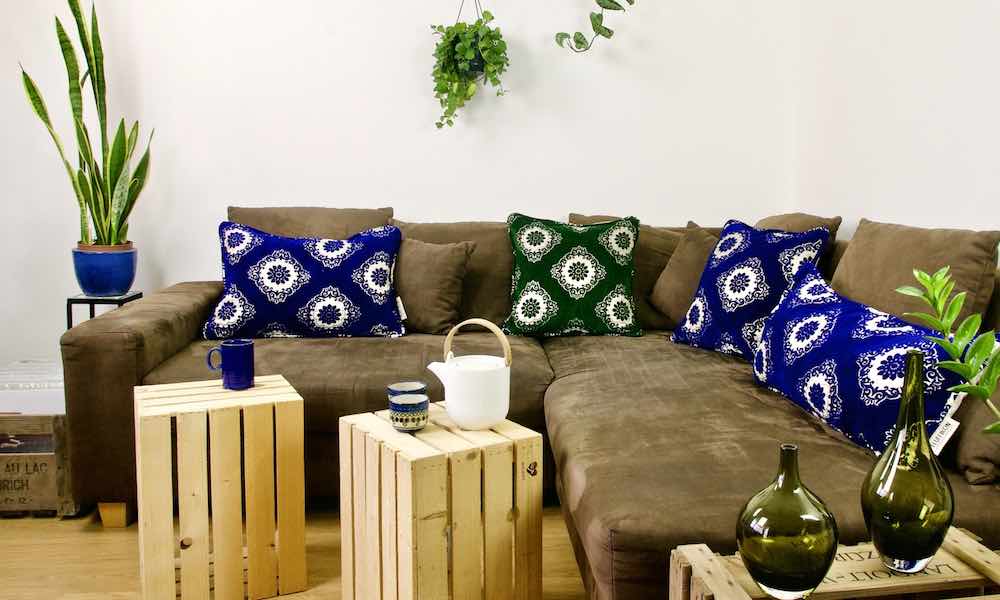 One green and three blue Moroccan pillows on a brown couch. 