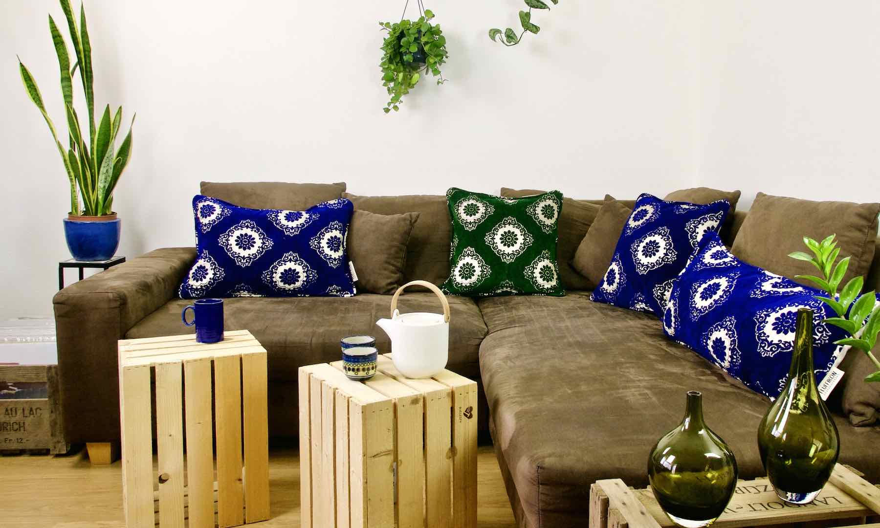 One green and three blue Moroccan pillows on a brown couch. 
