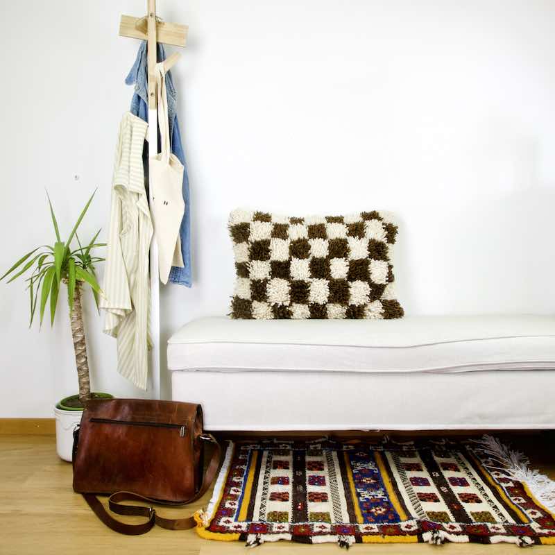 Braun weiss kariertes marokkanisches Dekokissen steht auf einer weissen Bank in einem Wohnzimmer. Ein marokkanischer Teppich liegt vor der Bank.