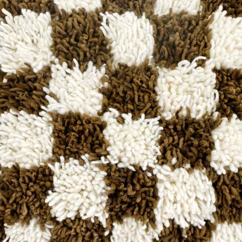 Detailed zoom on wool texture of earthly brown checkered Fluffikon Berber pillow.