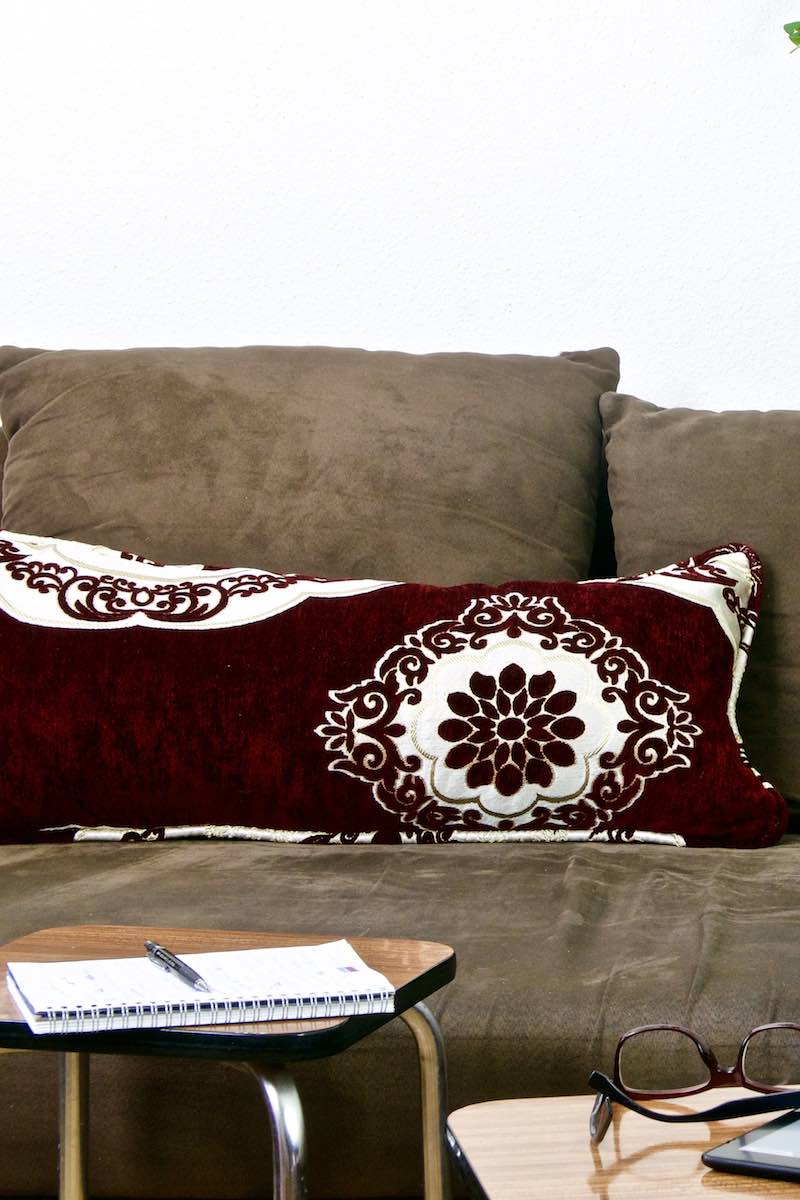 A burgundy red Fluffikon pillow on a brown couch. The pillow has traditional Moroccan patterns.