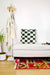 Checkered Moroccan Fluffikon pillow standing on a white bench. A red carpet is in front of the bench.