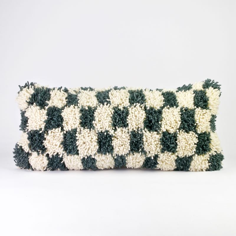 A checkered Moroccan wool lumbar pillow. The lumbar pillow is made from a Beni Ourain Moroccan wool rug. It is standing in front of a white background.