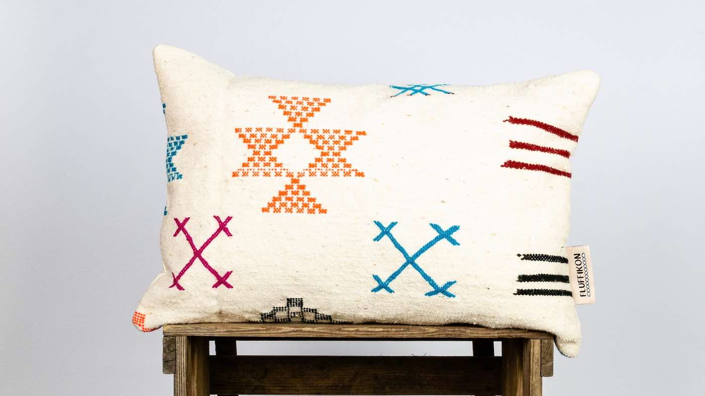 Colorful Fluffikon Kilim rectangular pillow on wooden box. The pillow has Berber symbols on it.