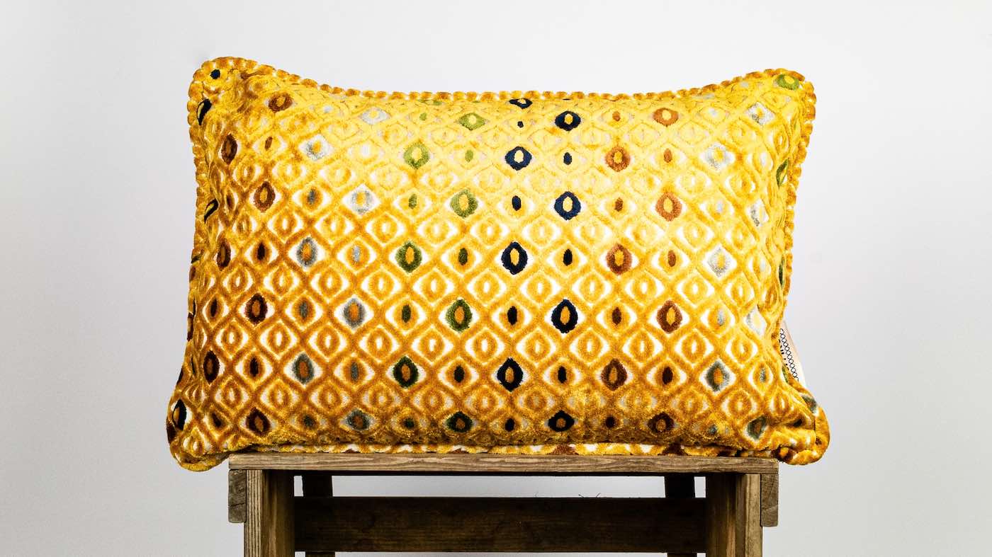 Mustard yellow Fluffikon cushion on wooden box.