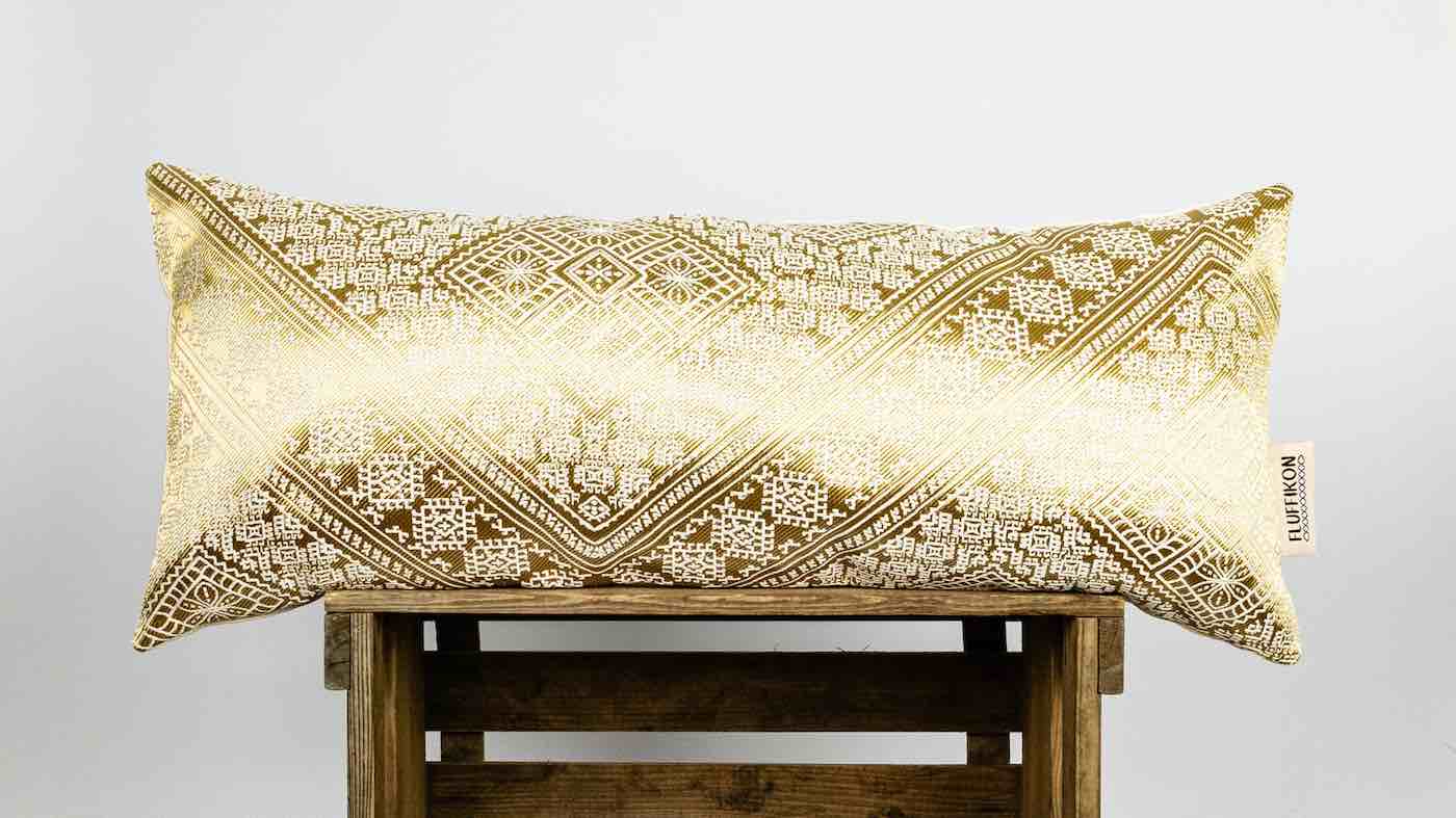 Fluffikon golden silk pillow in lumbar size standing on wooden box.