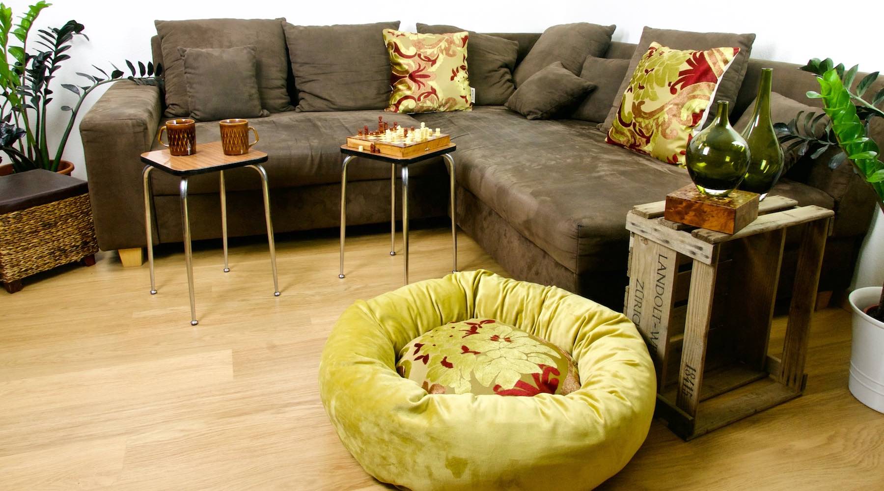 Red golden unique Fluffikon donut dog bed in an stylish living room. Two decorative pillows on the couch are made from the same material as the calming dog bed.