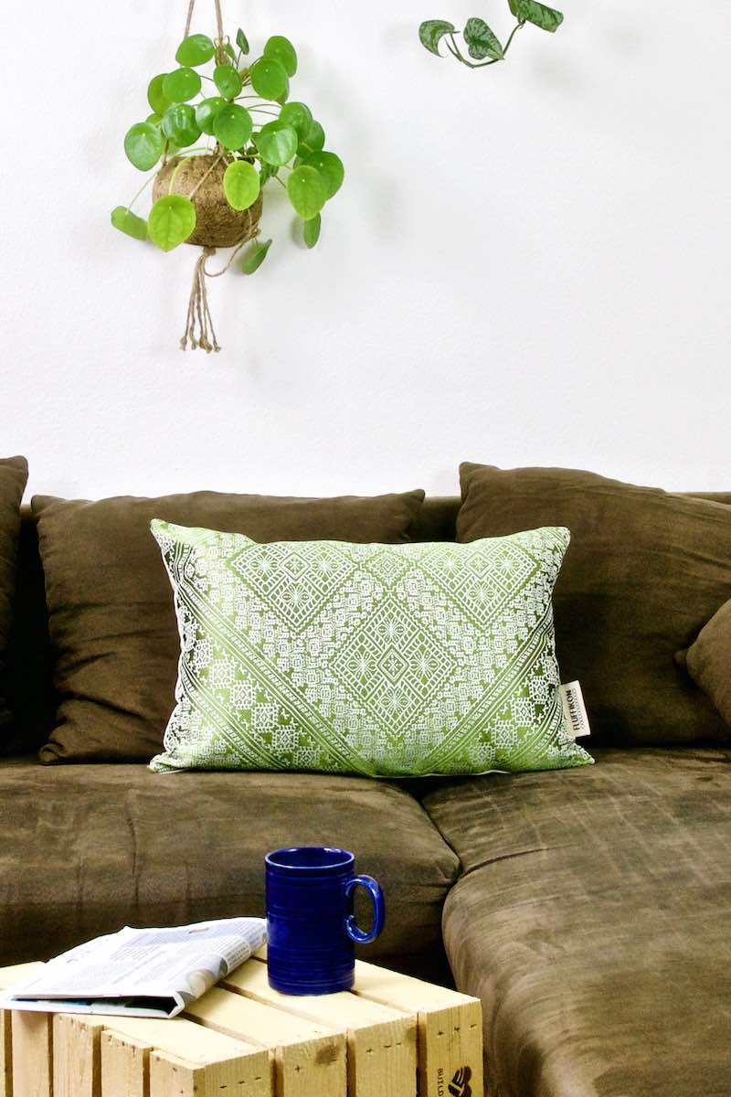 A green Fluffikon silk pillow with Moroccan pattens on a brown sofa.