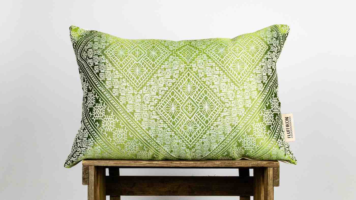 Green Fluffikon silk pillow that stands on a wooden box.